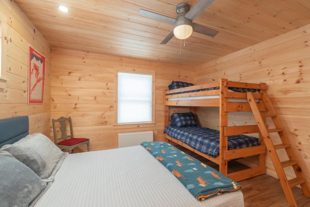 Bedroom with queen bed and bunk beds, knotty pine walls