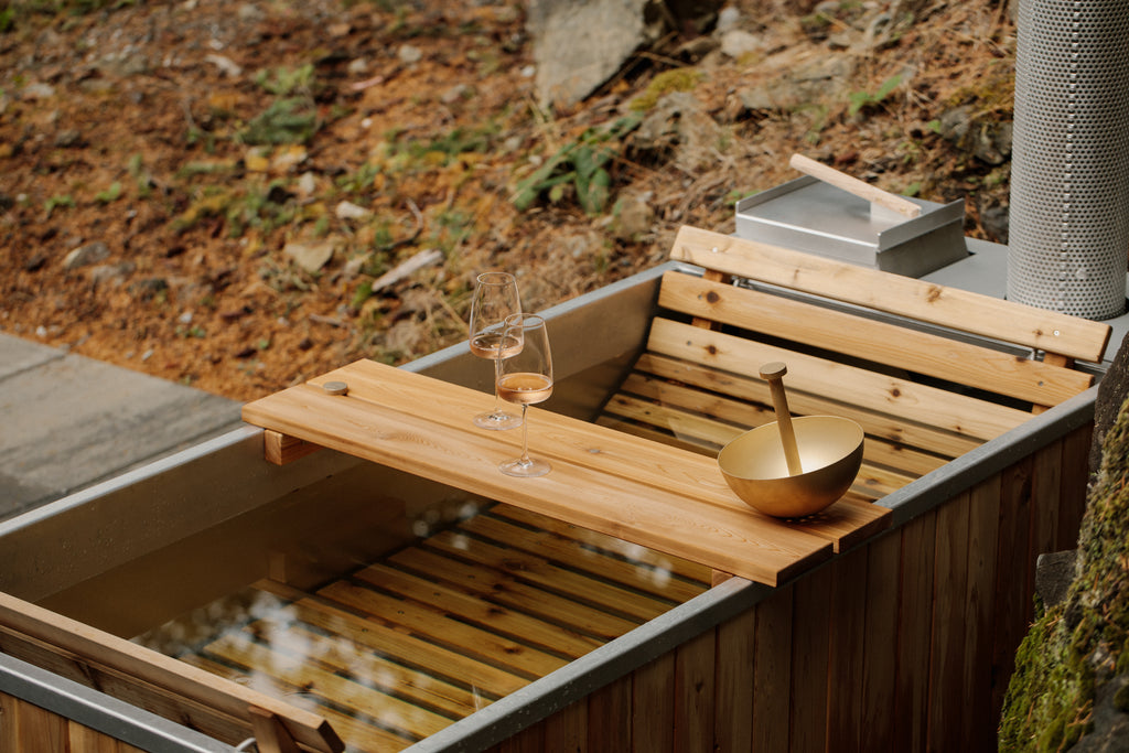 Wood-fired outdoor hot tub surrounded by nature with bath tray and hand shower