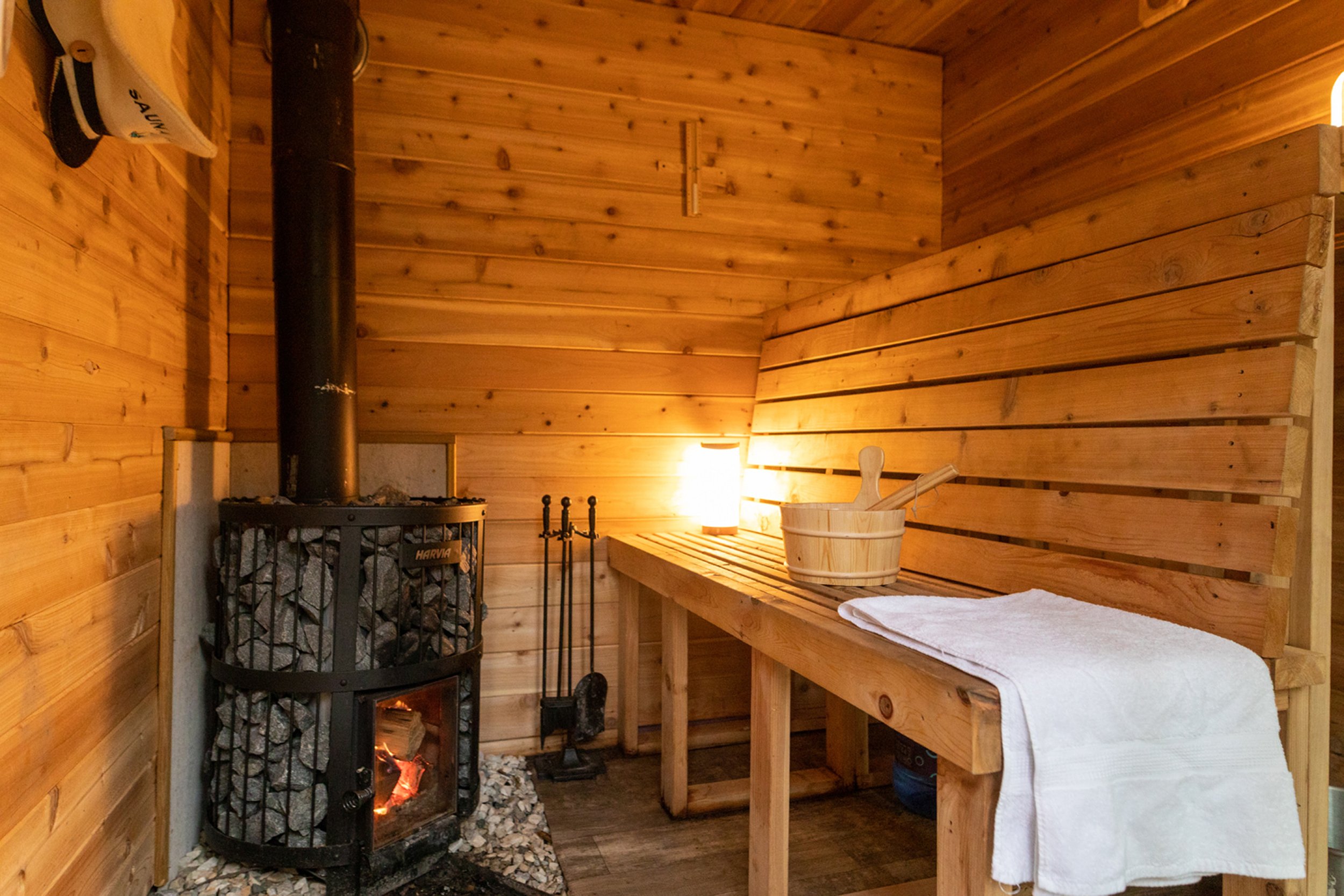 Wood-fired sauna interior with glowing fire, cedar benches and wooden bucket